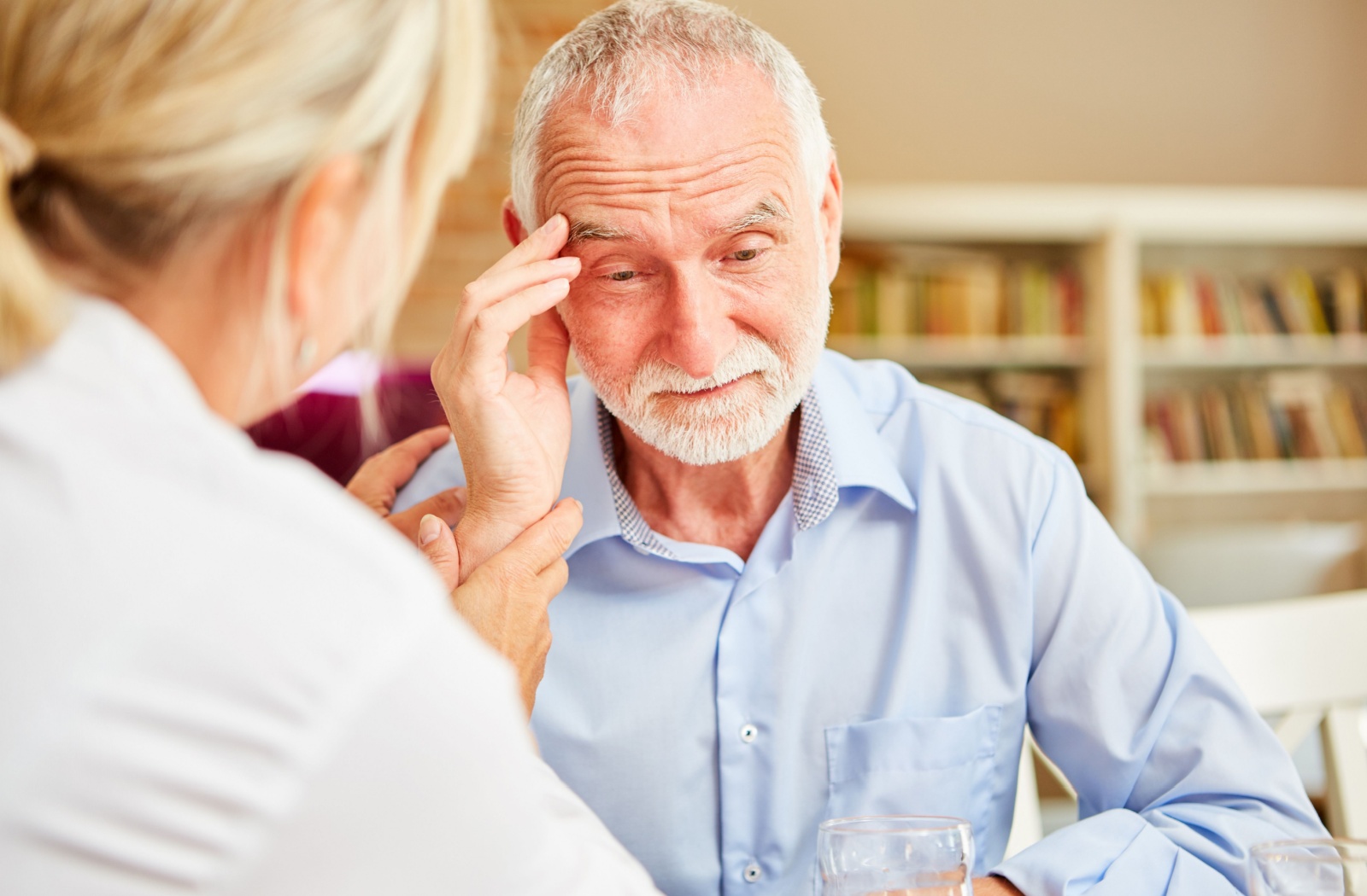 A caregiver reassures an older adult with dementia in their home
