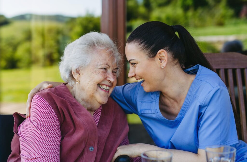 A caregiver and an older adult laugh together in a sunroom in memory care