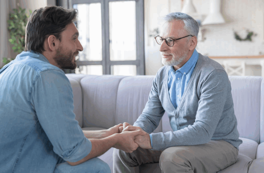 An older adult and their adult child holding hands and sitting across from each other during a conversation in senior living.