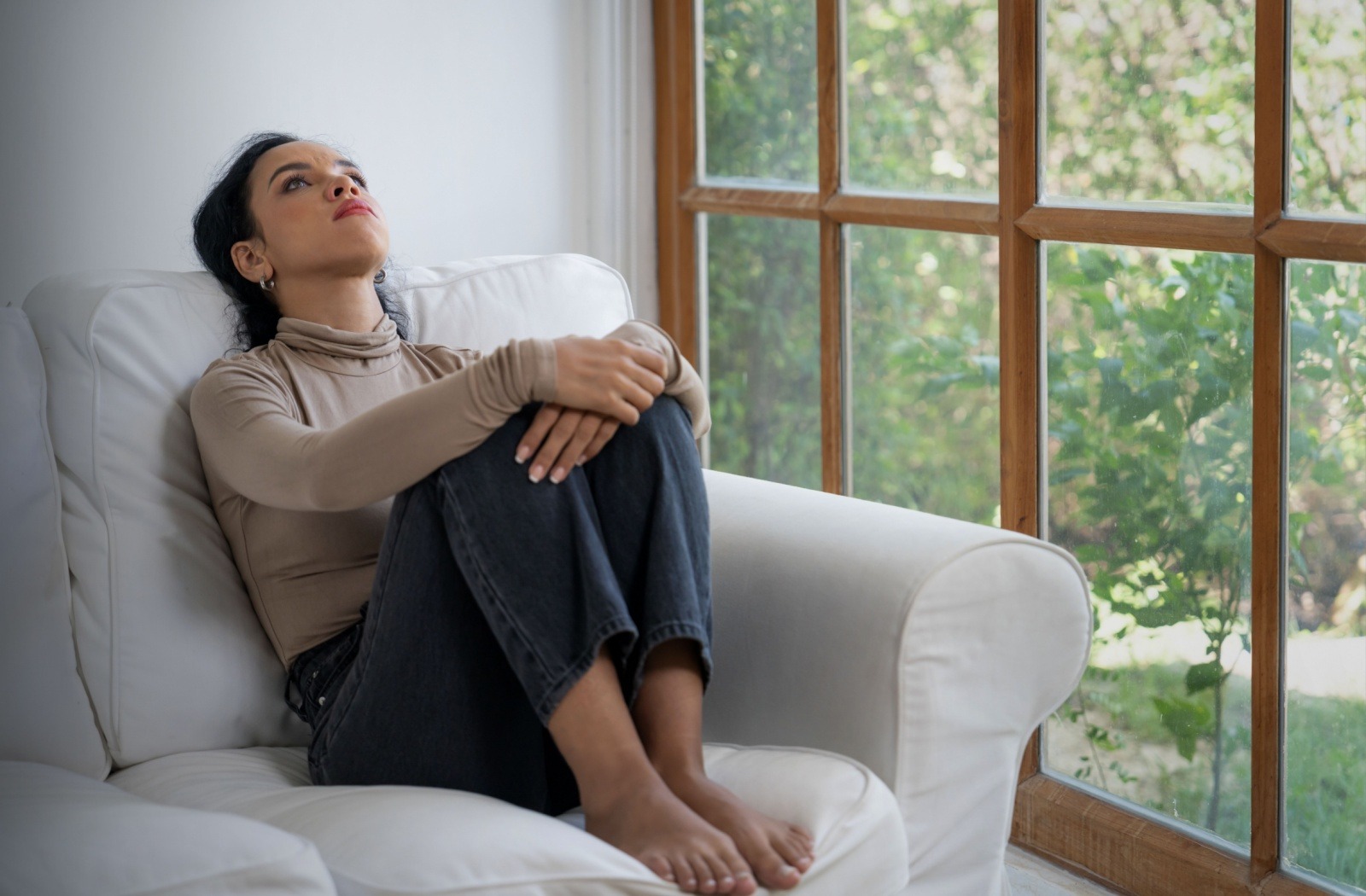 An exhausted caregiver relaxes on a white couch holding their knees