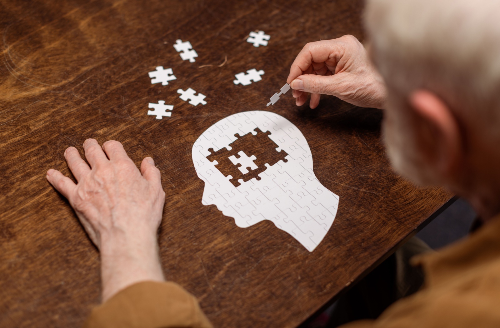 An older adult builds a puzzle in the shape of a human head, symbolizing improving memory.