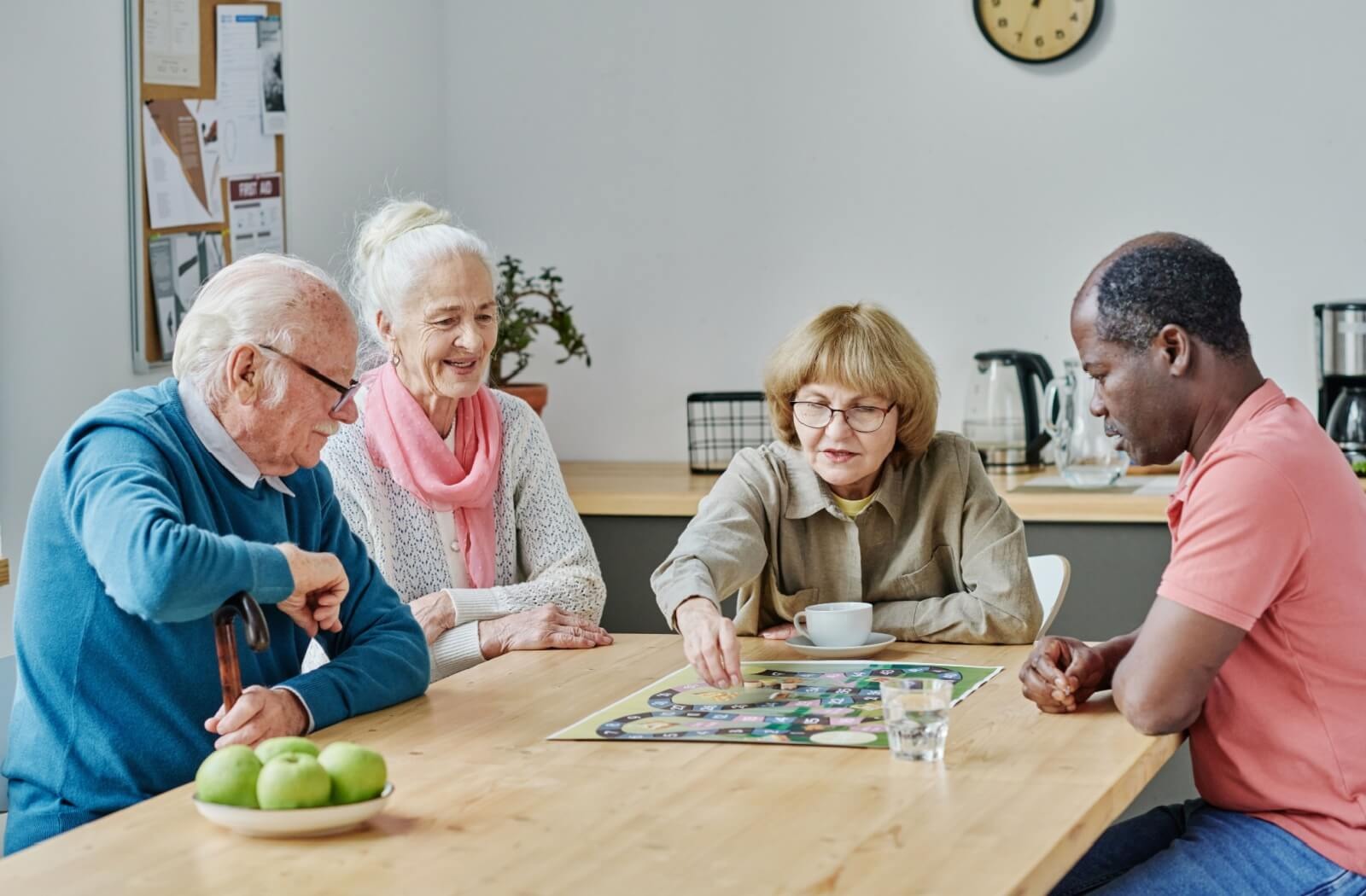 A group of older adults in senior living work play a board game together over tea