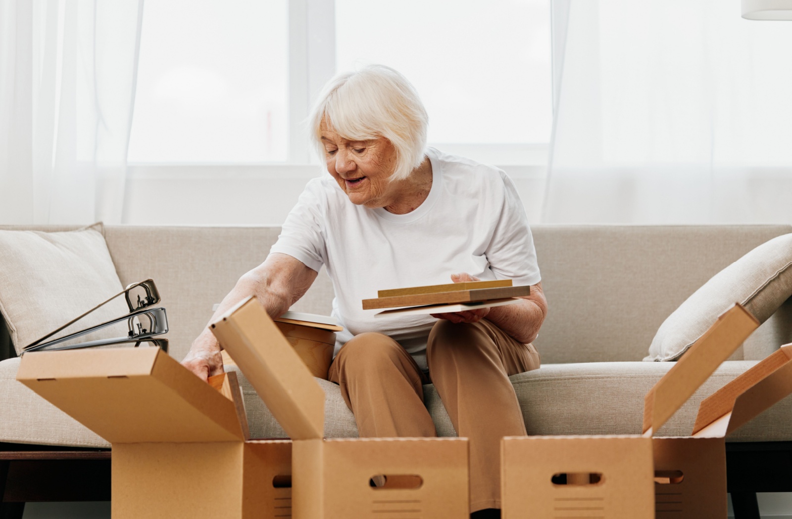 A senior sitting on a sofa looking through files and possessions with moving boxes in the foreground