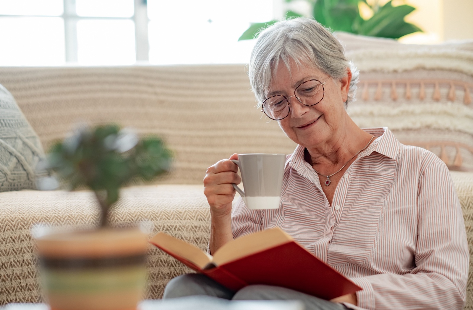 A senior sips a cup of coffee while reading a hardcover novel.