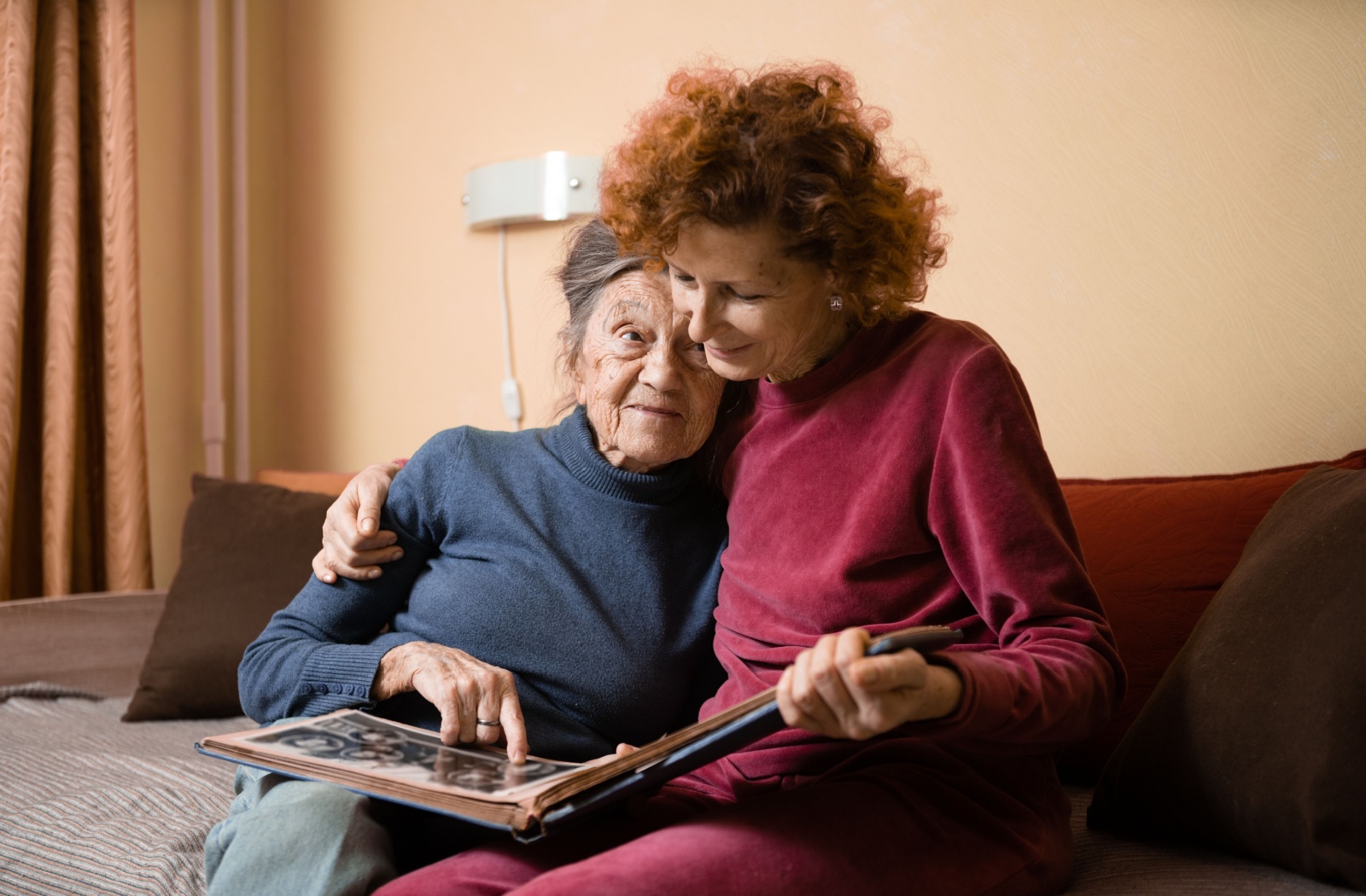 An adult child and their parent with dementia reminisce together while looking through a photo album.